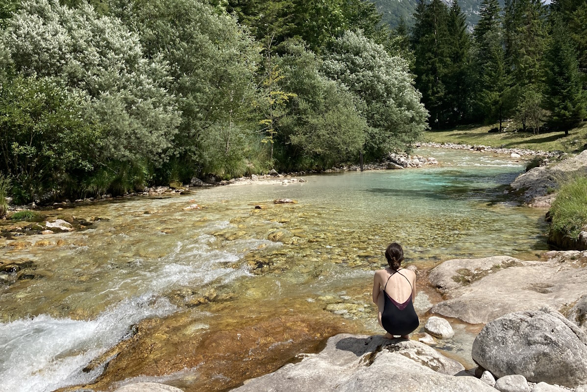 Eine Frau sitzt am Ufer eines klaren Bergflusses in einer Berglandschaft