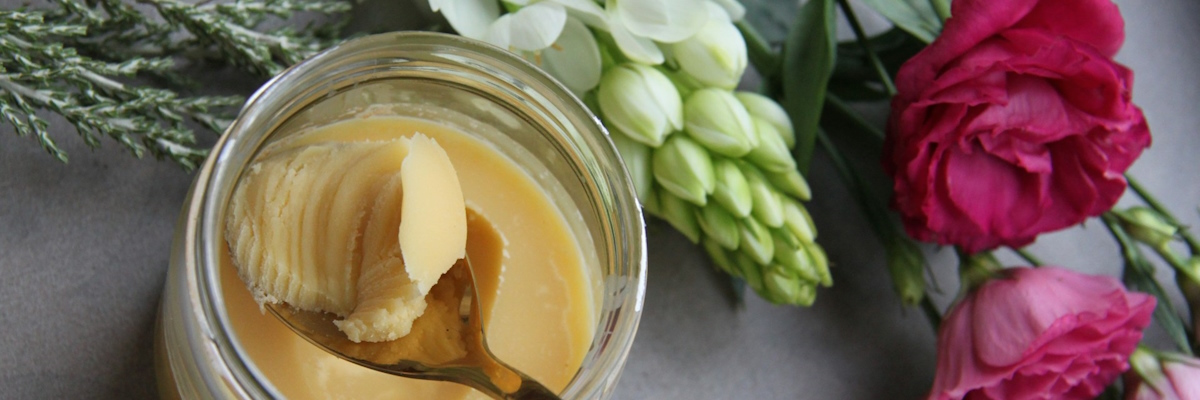 Ein Glas Ghee mit Löffel drin steht auf einem mit Blumen dekorierten Tisch