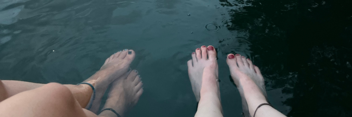 Um das Pitta-Dosha im Hochsommer zu senken, baumeln zwei Paar Füße an einem heißen Sommertag im kühlen Wasser eines Sees
