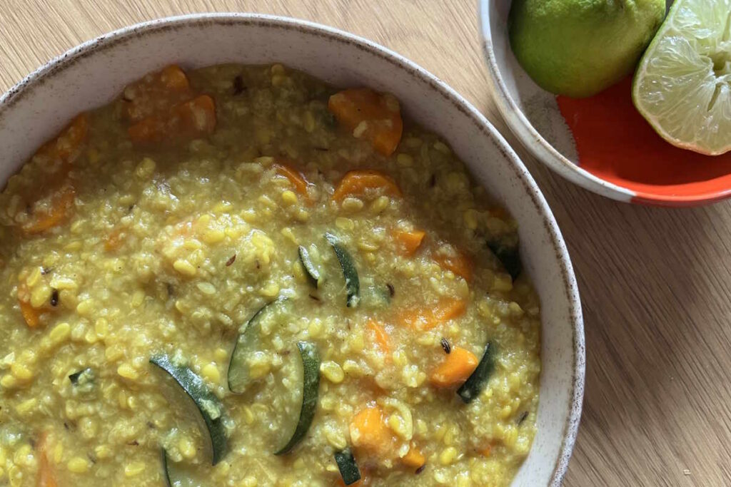 Der ayurvedische Eintopf Kitchari auf einem Teller, daneben eine kleine Schale mit angeschnittener Limette