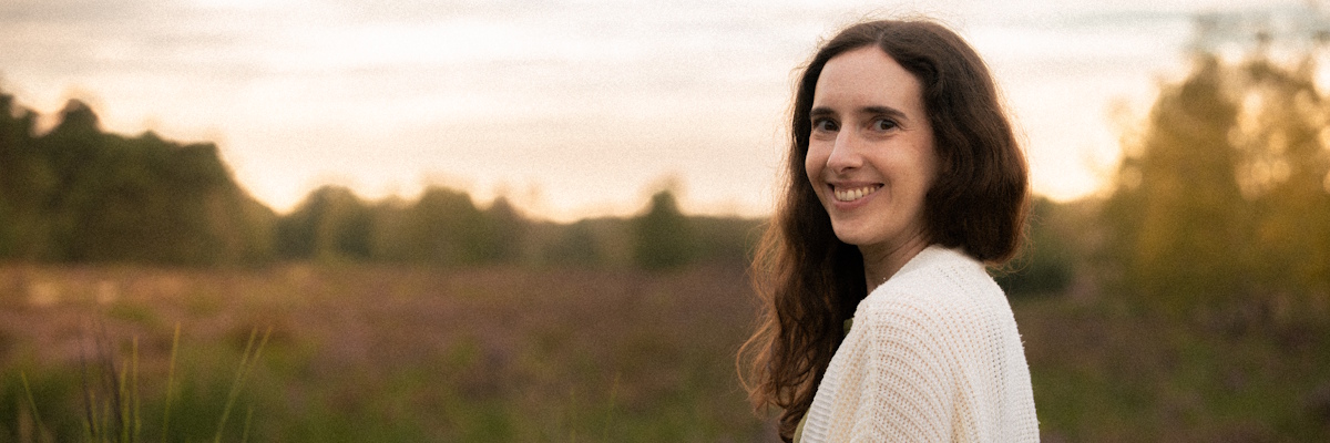 Ayurveda Beraterin Miriam, selbst Vata-Pitta-Typ, steht in einer blühenden Heide und dreht sich sanft zur Kamera um