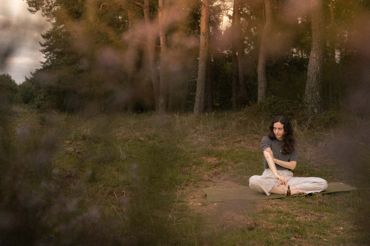 Ayurveda-Beraterin Miriam sitzt auf einer Lichtung vor dem Wald und ölt sich die Arme ein, denn Ölmassagen sind Teil des ayurvedischen Lebensstils