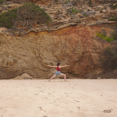 Ayurveda Beraterin und Yogalehrerin Miriam Sommer steht vor einer Felswand am Strand und praktiziert den Krieger 2