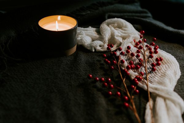 Eine brennende Kerze, eine Decke und ein herbstlicher Ast drücken Gemütlichkeit und Entspannung im Herbst aus - aus Sicht des Ayurveda wichtig, um Vata und Pitta in Balance zu halten